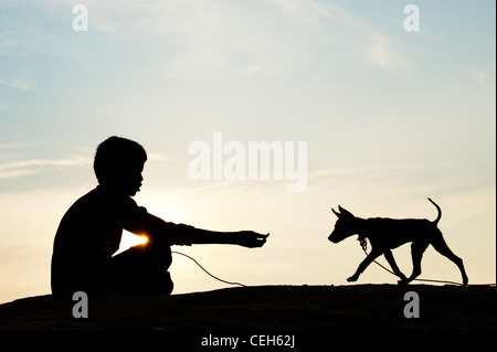 Silhouette di un giovane ragazzo indiano seduto e giocare con il suo cucciolo. India Foto Stock