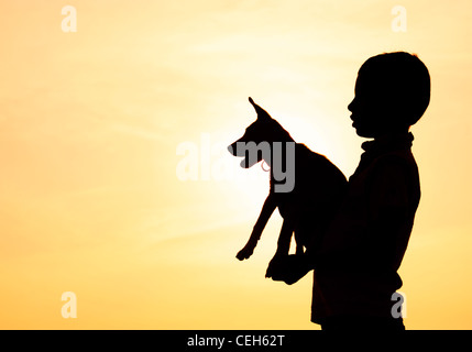 Silhouette di un giovane ragazzo indiano holding e giocare con il suo cucciolo. India Foto Stock