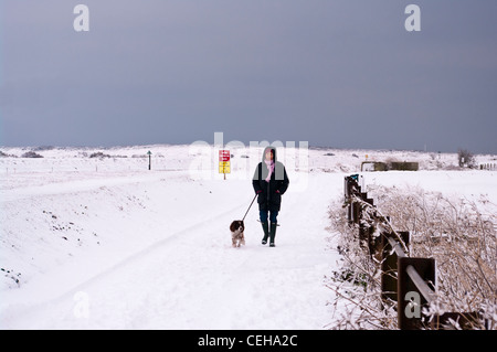 Vista frontale di una donna persona passeggiate con il suo cane nella neve invernale CAMPAGNA DEL REGNO UNITO Foto Stock