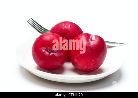 Tre prugne rosso su sfondo bianco Foto Stock