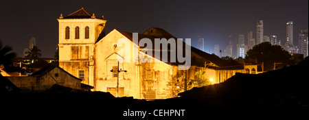 Un vecchio era coloniale chiesa prima lo sfondo di Cartagena del moderno skyline incandescente nella notte. Foto Stock