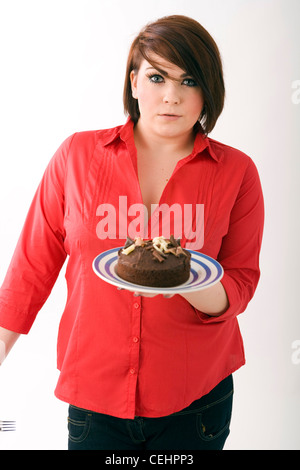 Leggermente sovrappeso donna che indossa camicetta rossa in piedi tenendo un grande torta al cioccolato. Foto Stock