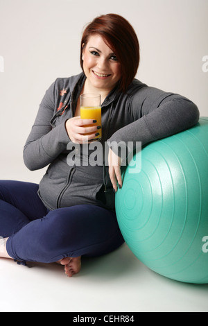 Donna braccio di appoggio sulla palla ginnica e tenendo un bicchiere di succo di arancia. Foto Stock