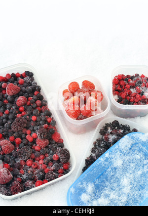 Contenitori di plastica di frutti di bosco misti congelati nella neve - still life Foto Stock