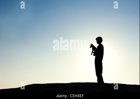 Silhouette di un giovane ragazzo indiano holding e giocare con il suo cucciolo. India Foto Stock