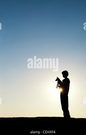 Silhouette di un giovane ragazzo indiano holding e giocare con il suo cucciolo. India Foto Stock