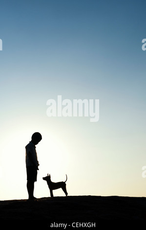 Silhouette di un giovane ragazzo indiano in piedi con il suo cucciolo. India Foto Stock