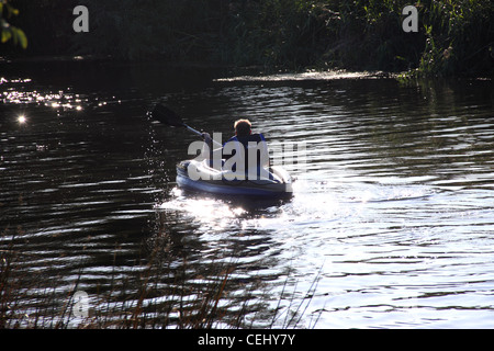 Un uomo che indossa un giubbotto di salvataggio pagaie un kayak lontano dalla fotocamera, spruzzi d'acqua da paddle, il fiume Avon, Bidford on Avon. Foto Stock