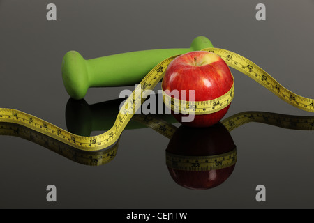 Red Apple, peso e nastro di misurazione isolata su un Riflettente superficie grigia Foto Stock
