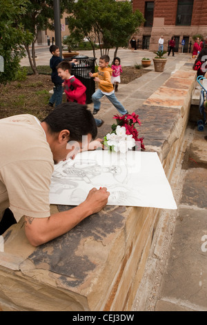 Giovane maschio ispanica artista lavora sul disegno a matita a un esterno di Plaza di San Antonio, Texas Foto Stock