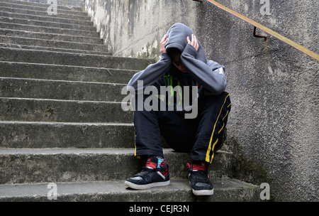 Un ragazzo adolescente sat con la sua testa in mani sui passaggi Foto Stock