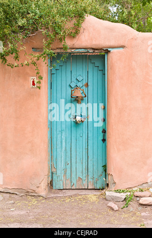 Un blu testurizzato porta di legno nella parete di adobe, con mail fuori della mailbox sulla porta, ricoperta bush appeso sulla parte superiore. Foto Stock