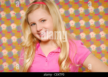 Close up ritratto di un sorridente ragazza di 10 anni con lunghi capelli biondi, in piedi di fronte a uno sfondo colorato. Foto Stock