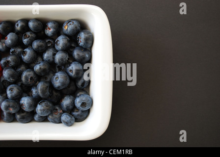 I mirtilli nel piatto bianco su sfondo grigio scuro, spazio libero per il testo a destra Foto Stock