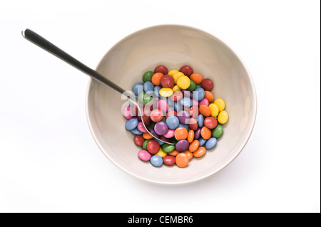 Ciotola con cucchiaio e caramelle colorate su bianco Foto Stock