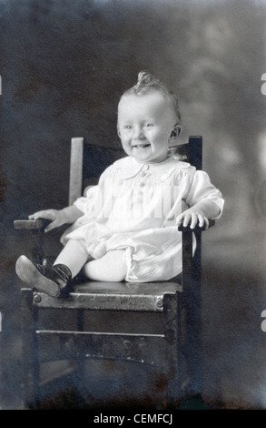 Un vintage fotografia di un bambino sorridente con un ricciolo sulla cima della sua testa, seduto in una sedia alta, circa 1909. Foto Stock