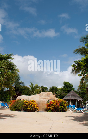 Splendida area piscina con grande pietra artificiale, sedie e bungalow in un resort tropicale circondata da palme) Foto Stock