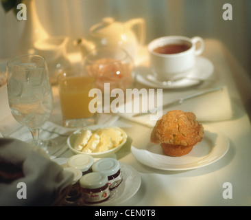 Prima colazione continentale in camera presso un hotel, spa, pasticceria con succo di frutta e tè, bicchiere vuoto con ghiaccio e rose in vaso Foto Stock
