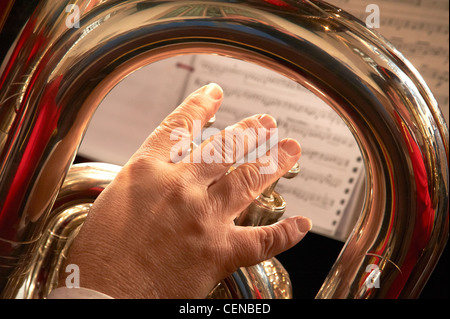 Dettaglio delle dita sulle valvole di bass strumento in ottone, con vista attraverso al foglio di musica. Foto Stock