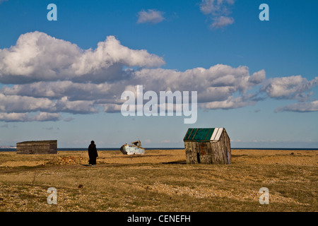 La donna a piedi passato abbandonato barche da pesca sulla spiaggia di Dungeness Foto Stock