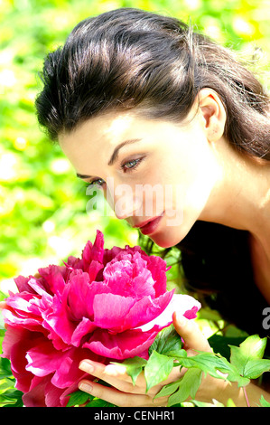 Close up semi del profilo femmina ondulata lungo brunette capelli appuntata faccia off tenendo un grande e luminoso rosa peonia appoggiata all'odore Foto Stock