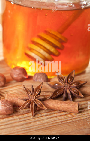 Stelle di anice e bastoncini di cannella a sinistra nella parte anteriore di un vasetto di miele con cucchiaio di miele in esso. Foto Stock