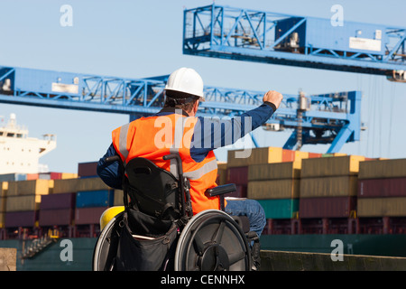 Ingegnere di trasporto in una sedia a rotelle a dare indicazioni per i contenitori di spedizione al porto di spedizione Foto Stock