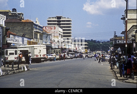 Scena occupato su Kenyatta Avenue Nakuru Kenya con il traffico di persone veicoli uomini donne auto parcheggiate negozi chimici Foto Stock