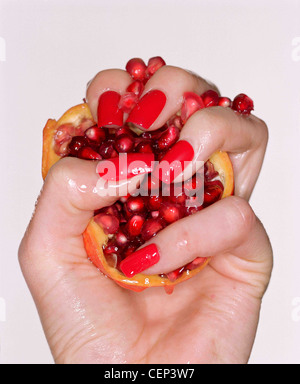 Indossare femmina rosso brillante smalto per unghie schiacciando un melograno nel palmo della sua mano Foto Stock