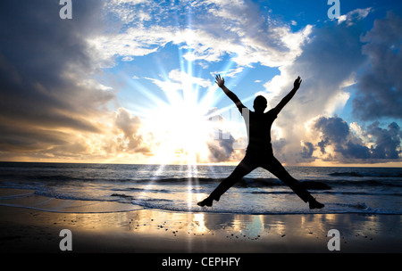 Uomo felice salto sulla spiaggia con bellissima alba Foto Stock