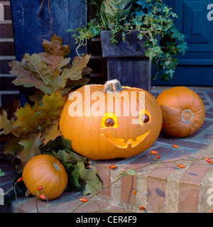 Grande zucca intagliata sorridenti faccia, occhi di castagno e illuminato tealight interno, sul gradino di pietra al di fuori davanti casa doof, due piccoli Foto Stock