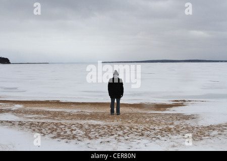 Un uomo solitario in piedi su una spiaggia innevata e guardando in lontananza. Foto Stock