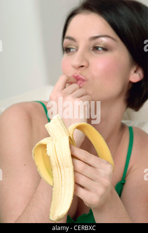 Femmina con lunghezza mento dritto brunette capelli mangiando una banana, e succhiare il suo dito Foto Stock