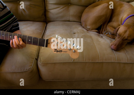 Ragazzo a suonare la chitarra mentre il suo cane dorme accanto a lui Foto Stock