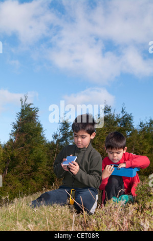 Due ragazzi di trovare un tesoro di geocache in cappe Foto Stock