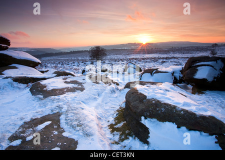 Il tramonto visto dalla coperta di neve su Owler Tor nel Parco Nazionale del Peak District. Foto Stock
