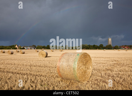 Vista su balle di fieno verso un arcobaleno su Santa Trinità e Chiesa di tutti i santi a Winterton-on-Sea. Foto Stock