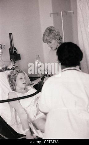 SE solo le donne capelli biondi indossa bianco Gilet tirato fino oltre la gravidanza stomaco giacente sul letto di ospedale gli occhi chiusi di dare la nascita Foto Stock