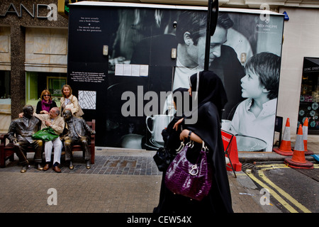 Donna araba, oltrepassando un cartellone pubblicitario nel West End di Londra Foto Stock