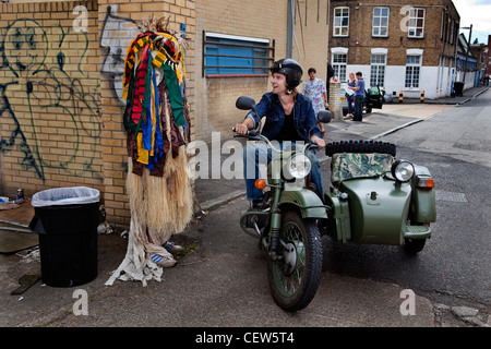 Uomo che indossa tribali costume headless in Hackney Wick Festival parlando di un uomo su una moto con sidecar. Foto Stock