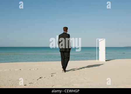 Imprenditore camminando sulla spiaggia verso la semi-porta aperta in background Foto Stock