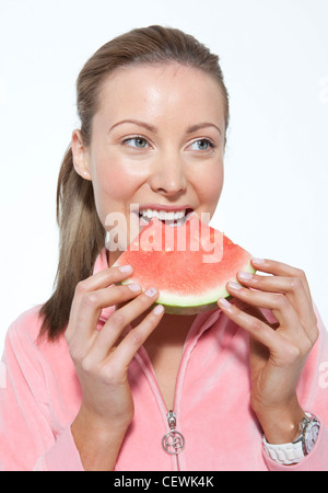 Femmina con capelli biondi legati a coda di cavallo, indossa una camicia rosa, mangiando anguria, sorridente, guardando al lato Foto Stock