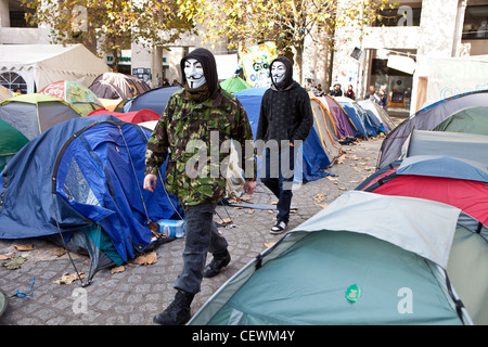 Manifestanti mascherati a piedi tra le tende di occupare Londra OSLX protesta a San Paolo. Foto Stock