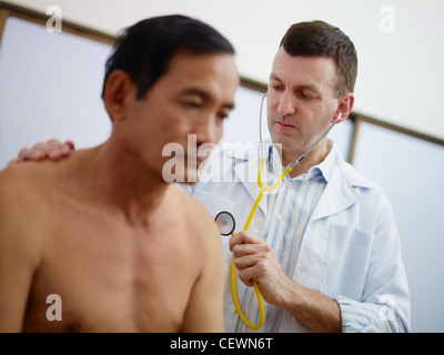 Medico caucasica lavorando e visitando il vecchio asian paziente di sesso maschile in ospedale con uno stetoscopio Foto Stock