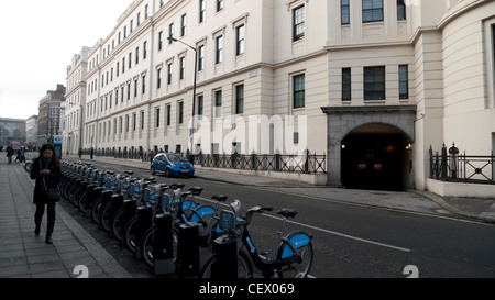 Una donna che cammina ultimi appartamenti e una fila di biciclette a noleggio biciclette presso una stazione docking su Guglielmo IV San in London WC2 UK KATHY DEWITT Foto Stock