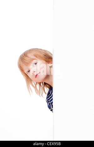 Curioso ragazzo con lunghi capelli biondi che spuntavano da dietro un pannello bianco cercando Foto Stock