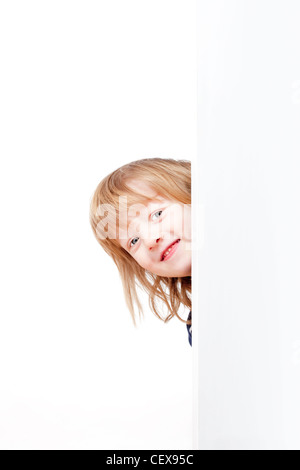 Curioso ragazzo con lunghi capelli biondi che spuntavano da dietro un pannello bianco cercando Foto Stock