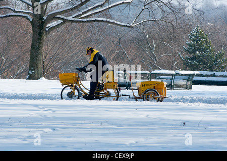 Un postino tedesco in bicicletta attraverso la neve nel Parco Olimpico, Monaco di Baviera, Germania. Foto Stock