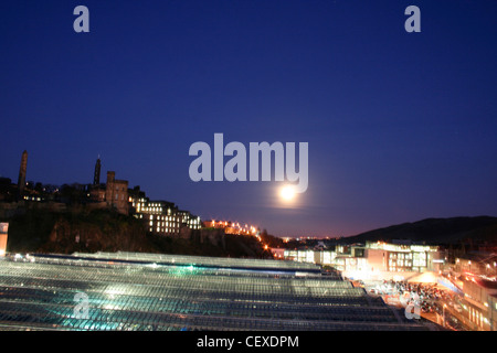 Vista sulla stazione di Edinburgh Waverley dal North Bridge skyline di Calton Hill grande notte di luna cielo blu scuro con retroilluminazione tetto di vetro Foto Stock