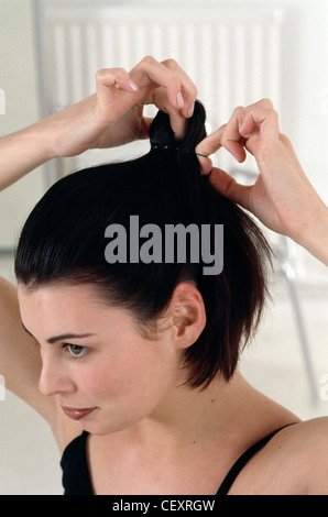 Passo per passo i capelli Updo femmina con brunette capelli, legando i suoi capelli in coda di cavallo, c'erano pochi sorrisi, cercando in distanza Foto Stock